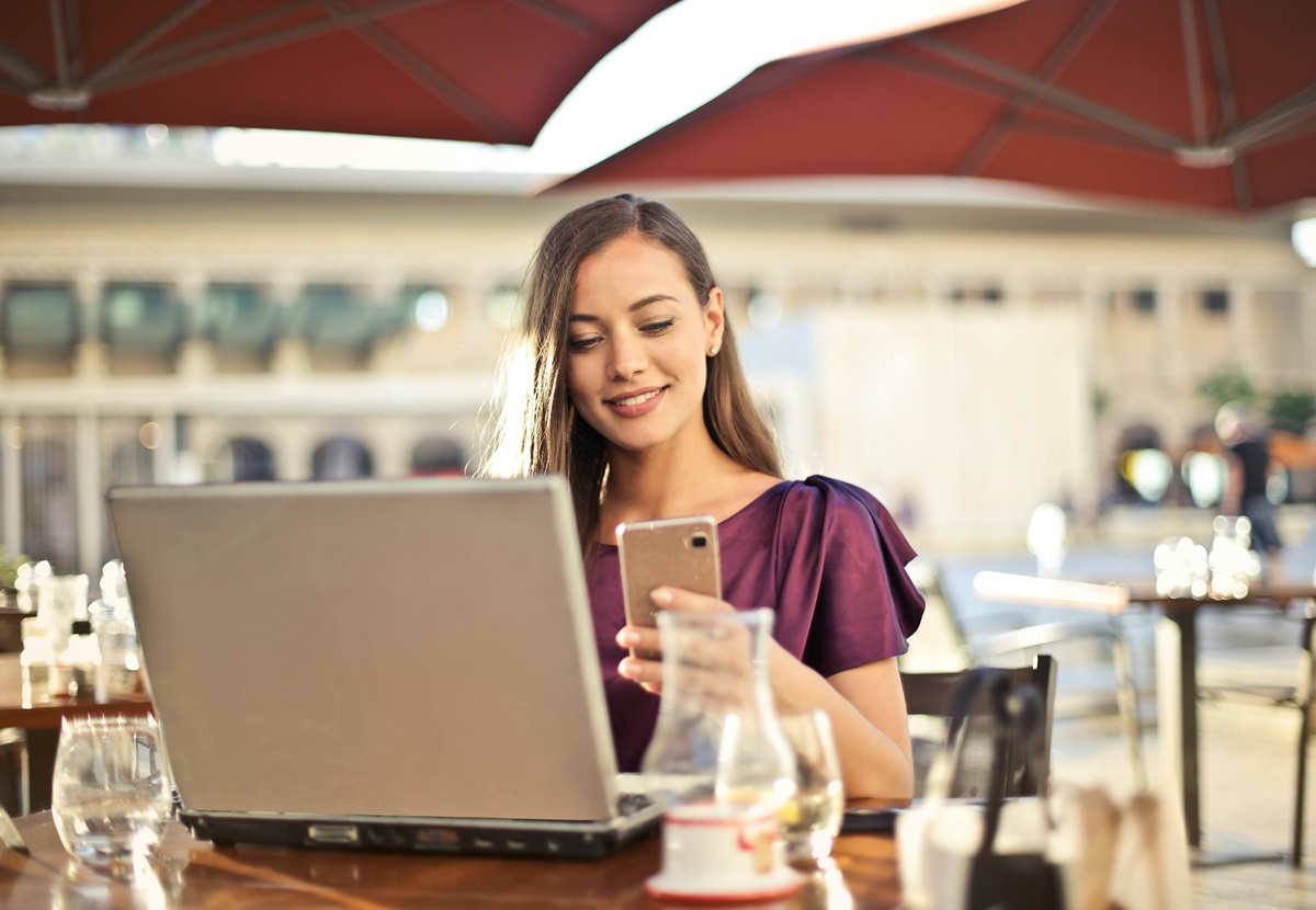 woman in shop sitting looking at laptop and smartphone in hand