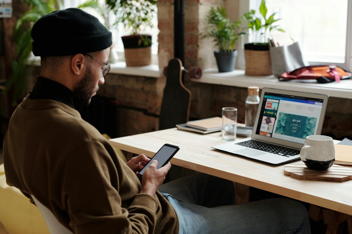 a freelancer is a better option for your web design needs and this man in ski hat looking at phone in front of computer desk is a local freelancer