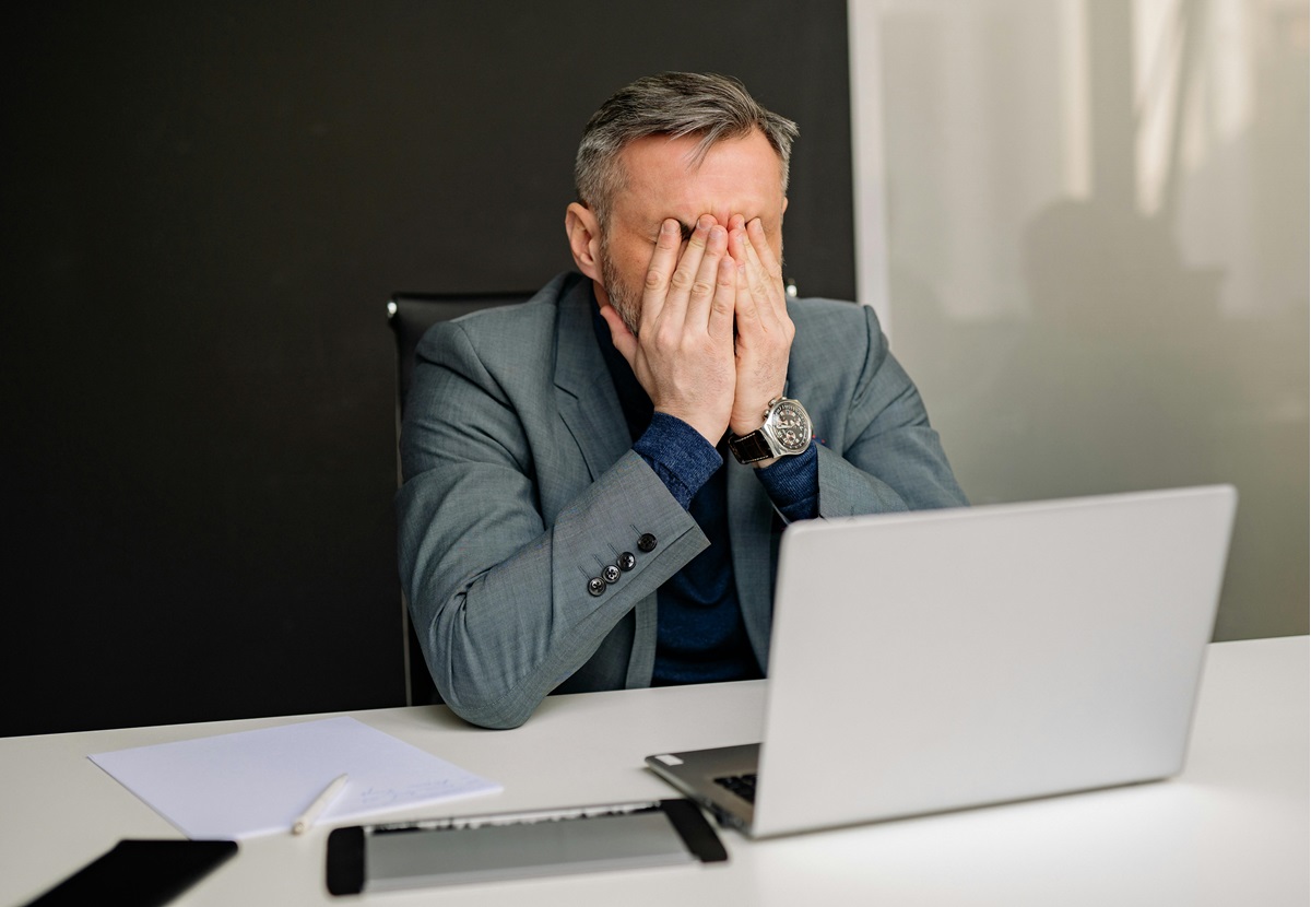 frustrated man neglecting WordPress maintenance tips rubbing eyes staring at laptop on desk